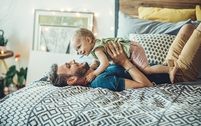 dad and daughter playing on bed in bedroom