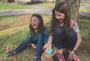 two kids laughing and sitting near a tree