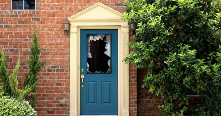 Close-up shot of broken window glass in teal front door of brick house