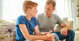 Featured father talking to son on couch