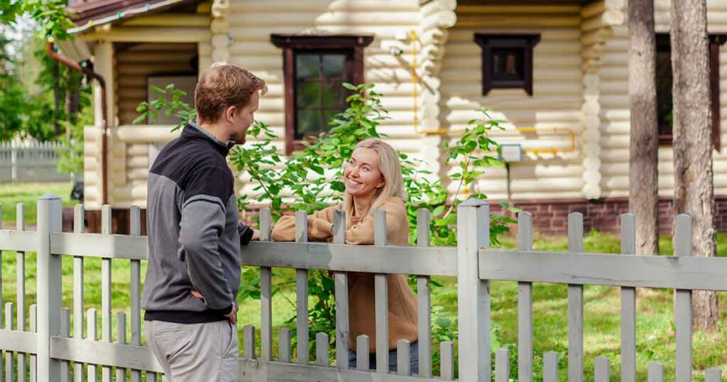 two neighbors conversing over a fence outside