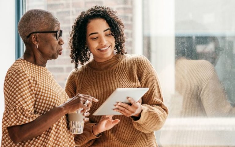 adult showing senior woman how to use something on a tablet