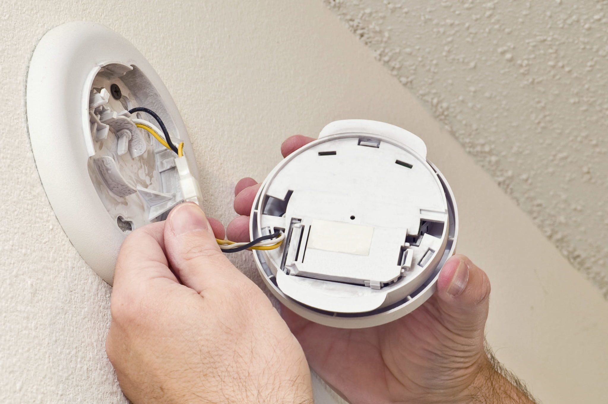 A workman performs regular maintenance on a smoke alarm.