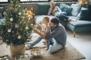 dad and baby decorating christmas tree on the floor, mom watching on the couch