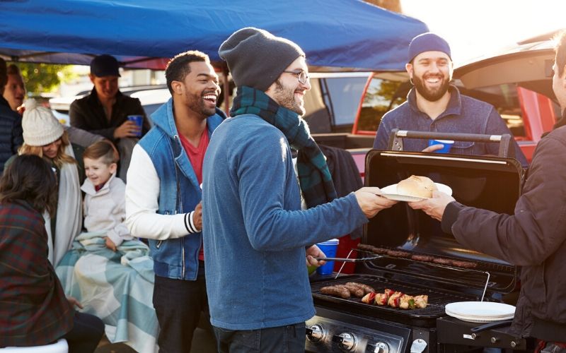 sports fans grilling hot dogs in a parking lot