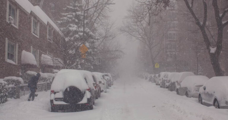 Man trying to clear snow on sidewalk and cars buried in snow in Brooklyn NY